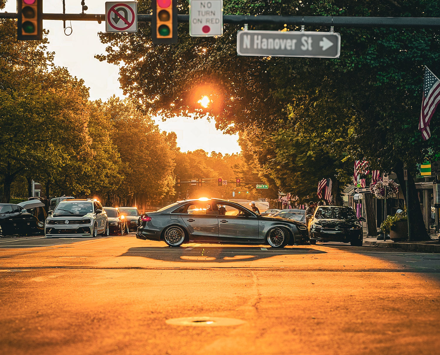 Car event street scene featuring multiple modified Volkswagen at a set of traffic lights with a lowered Audi on BBS wheels passes through the frame, during sunset,