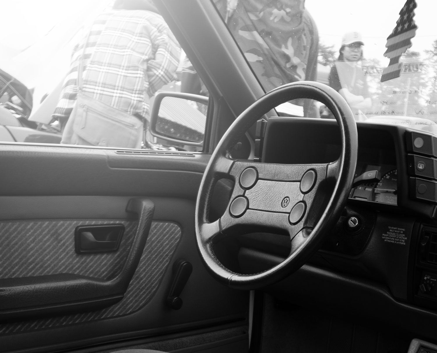 Black and white steering wheel and dashboard of a Volkswagen Fox with a busy background of people at a car show